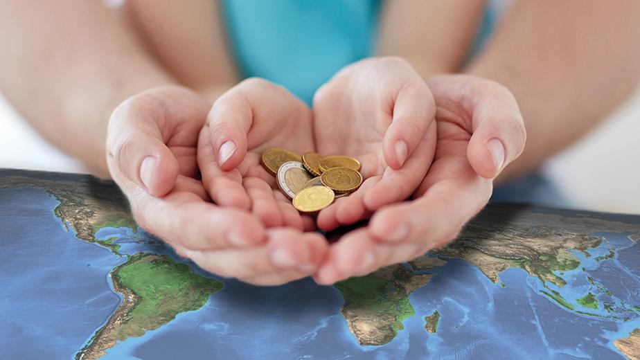 Die Hände eines Kindes liegen in den geöffneten Händen eines Erwachsenen, die auf einer Weltkarte aufliegen. In den Händen des Kindes liegen Geldmünzen.